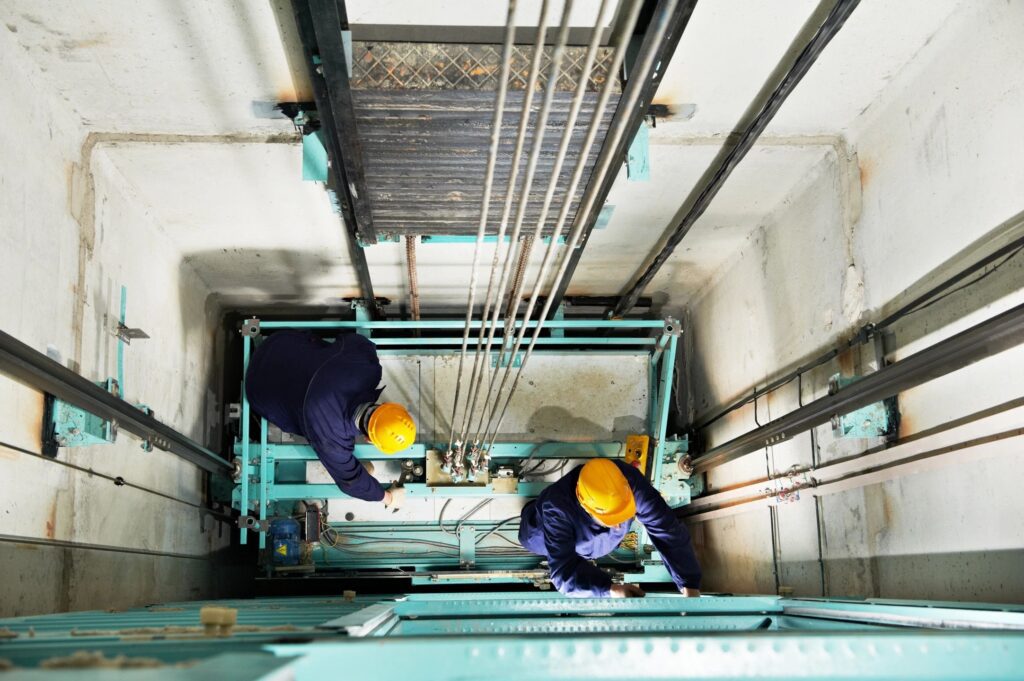 Two workers inspecting elevator shaft machinery.